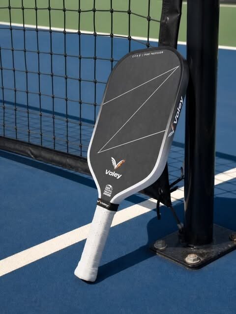 Voley pickleball paddle resting against a court net