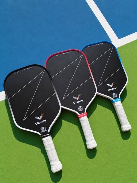 Three Voley pickleball paddles lying on a court